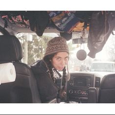 a man sitting in the back seat of a car wearing a knit hat and scarf