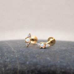 two small white and yellow gold earrings on top of a black stone surface, with one diamond set in the middle