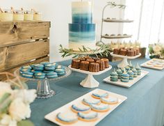 a table topped with cakes and cupcakes next to a cake stand filled with cookies