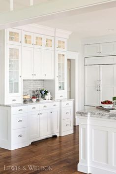 a large kitchen with white cabinets and marble counter tops, along with hardwood floorsing