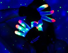 two hands with neon lights on them are in the dark, and one is wearing black gloves