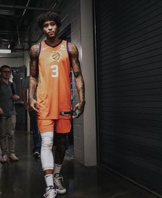 a man in an orange basketball uniform is walking down the street with his hands on his hips