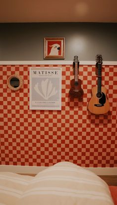 guitars are hanging on the wall next to a bed in a room with checkered walls