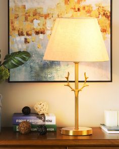 a lamp on a table next to books and a vase with a plant in it