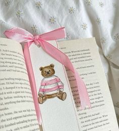 an open book with a pink ribbon on it and a teddy bear in a sweater