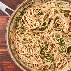 a pan filled with pasta and parsley on top of a wooden table