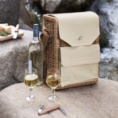 a bottle of wine and two glasses sitting on top of a rock next to a basket