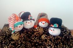 three knitted snowmen sitting on top of pine cones