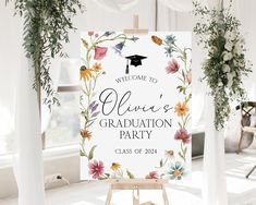 a welcome sign with flowers and graduation cap on it in front of white drapes