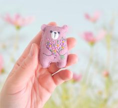 a hand holding a small purple teddy bear with flowers on it's chest and eyes