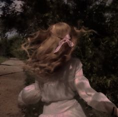 a woman with long red hair walking down a sidewalk next to a tree filled park