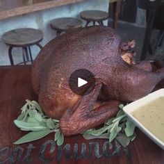 a large turkey sitting on top of a wooden table next to a bowl of gravy