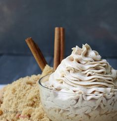 a bowl filled with whipped cream next to cinnamon sticks