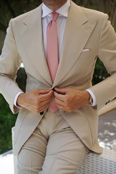 a man in a tan suit and pink tie is sitting on a white bench with his hands behind his back