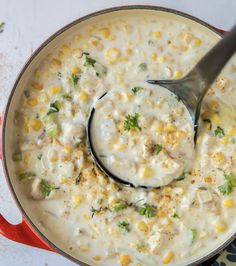 a red pot filled with corn chowee and a ladle full of the soup