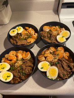 four black pans filled with food on top of a kitchen counter next to a stove