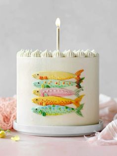 a birthday cake decorated with colorful fish on it's side and two candles in the middle