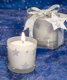 two white candles sitting next to each other on a blue table cloth with silver stars