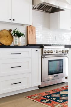 a kitchen with white cabinets and stainless steel stove top oven in the center, surrounded by potted plants