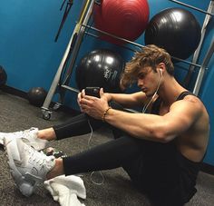 a young man sitting on the ground using his cell phone while listening to headphones