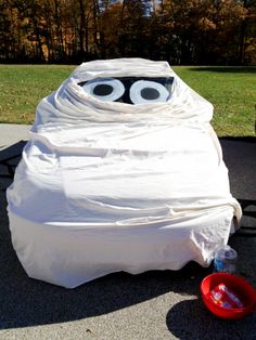 a white plastic bag with eyes on it sitting in the middle of a sidewalk next to a red bowl