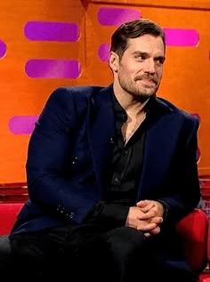 a man sitting on a red chair in front of an orange wall with purple letters