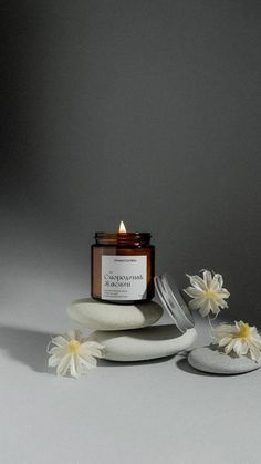 a candle sitting on top of a white plate next to some daisies and rocks