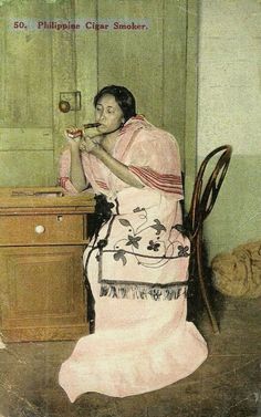 a woman sitting at a table with a spoon in her mouth and wearing a pink dress