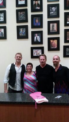 three men and a woman standing in front of a counter with pictures on the wall behind them