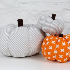 two pumpkins sitting next to each other on a white surface with a brick wall in the background