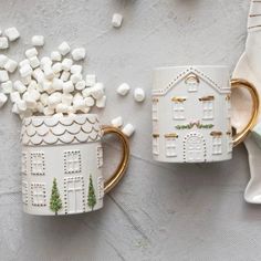 two coffee mugs decorated with white marshmallows and gold rimmed handles