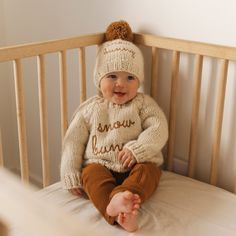 a baby sitting in a crib wearing a knitted sweater and hat with the words snow bunny written on it