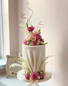 a wedding cake decorated with flowers and feathers on a white table next to a window