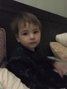 a little boy that is sitting in a bed next to a pillow and blanket on the floor