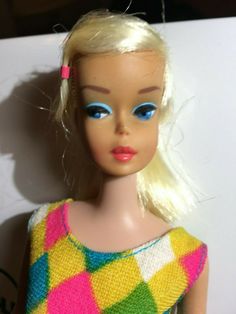 a doll with blonde hair and blue eyes wearing a multicolored dress on display