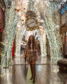 a woman is walking down the street in front of christmas lights and a large clock