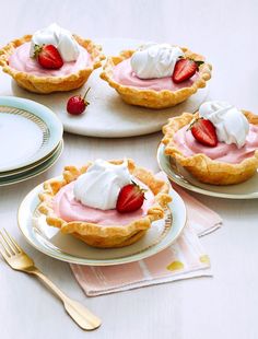 three small pies with whipped cream and strawberries on them are sitting on plates