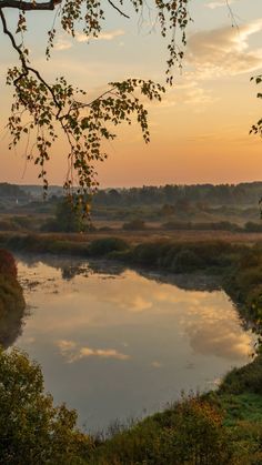 the sun is setting over a river with water and trees in the foreground,