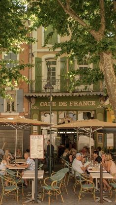 people sitting at tables under umbrellas in front of a building