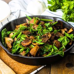 a pan filled with mushrooms and greens on top of a cutting board next to some bread