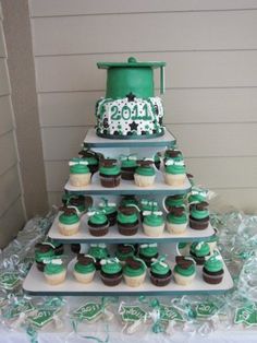 a cake and cupcakes are arranged on a tiered tray with green ribbons