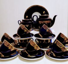 a group of black and gold tea cups and saucers with matching saucer sets