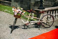 a bicycle with flowers in the basket parked next to a red carpet and stone wall