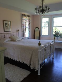 a white bed sitting in a bedroom on top of a hard wood floor next to a window