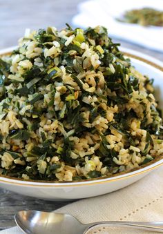 a bowl filled with rice and greens on top of a table next to silverware