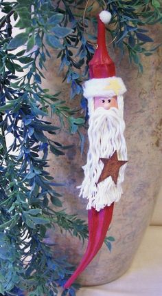 a santa clause ornament hanging from a tree branch with green leaves around it