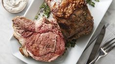 two steaks on a white plate with ranch dressing and a fork next to it