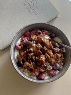 a bowl of cereal with chocolate and raspberries in it next to a notebook