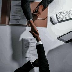 two people shaking hands over papers on a desk