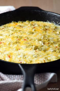 a skillet filled with cheese and vegetables on top of a table next to a towel